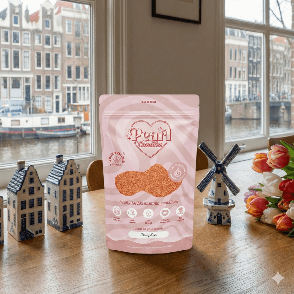 Pearl Candles verpakking met kaarsenzand op een houten tafel, geplaatst voor een raam met uitzicht op grachtenpanden, wat een stijlvolle en inspirerende setting creëert voor interieurdecoratie.